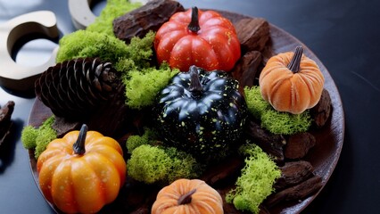 Orange, black pumpkins sit on green moss, red currants scattered, pine cone beside, rustic wood highlights autumn scene, vibrant colors evoke harvest warmth. Symbol of autumn abundance