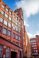 Fototapeta premium Manchester city center. Historic red brick mill building with tall windows under a clear blue sky.