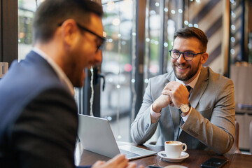 Two mid adult Caucasian men engaged in a business discussion at a cafe, one smiling as they...