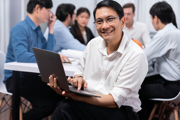 Fototapeta premium Confidence and happy smiling businessman portrait with background of his colleague and business team working in office. Office worker teamwork and positive workplace concept. Prudent