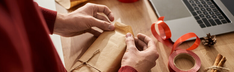 A young man carefully wraps a Christmas present at his workspace during the festive season.