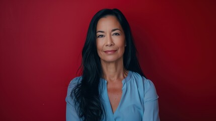 Fototapeta premium Professional Woman in Pastel Blue Blouse with Warm Smile Against Deep Red Background