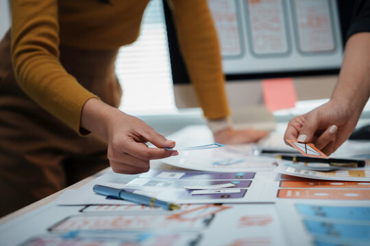 Web designers collaborate in an office, choosing colors for a mobile app interface, brainstorming, strategizing, and researching different color palettes
