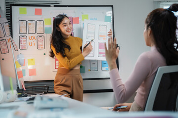 Two female web designers discussing user interface design during a meeting in a modern office,...