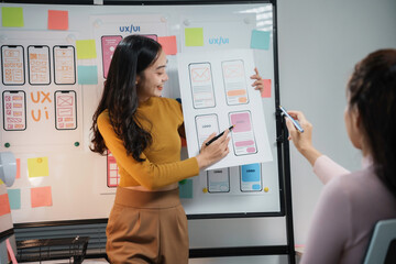 Two female ux ui designers are discussing mobile app interface design on whiteboard in the office