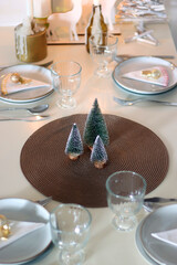 Table set for Christmas meal with plates, glasses, holiday decorations, lit candles and wine. Selective focus.