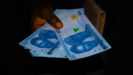 Black Female hand holding Nigerian Naira notes and pink purse over dark background, Currency of Nigeria
