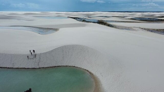 A drone reveals the vast white dunes of Len&ccedil;&oacute;is Maranhenses, with shimmering lagoons nestled between the rolling sands. The sweeping aerial view captures the stunning contrast of the endless desert.