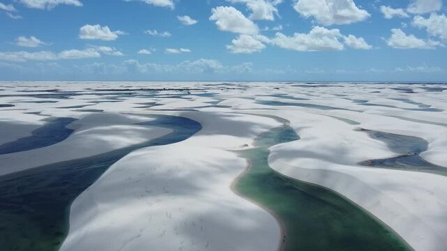 A drone reveals the vast white dunes of Len&ccedil;&oacute;is Maranhenses, with shimmering lagoons nestled between the rolling sands. The sweeping aerial view captures the stunning contrast of the endless desert.