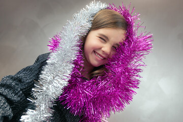 Cute little girl with funny expression playing with the tinsel. Christmas decoration