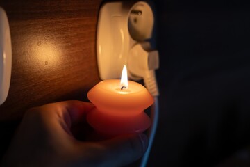 Burning candle in hand near socket in darkness. Power outage due to war in Ukraine