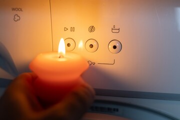 Burning candle in hand near washing machine in the dark. Power outage due to war in Ukraine