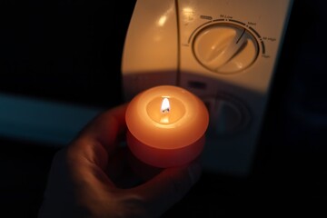 Burning candle in hand near microwave oven in dark. Power outage due to war in Ukraine