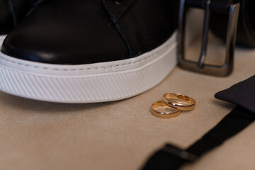 Sleek Black Sneaker Beside Wedding Bands and Accessories on a Neutral Surface