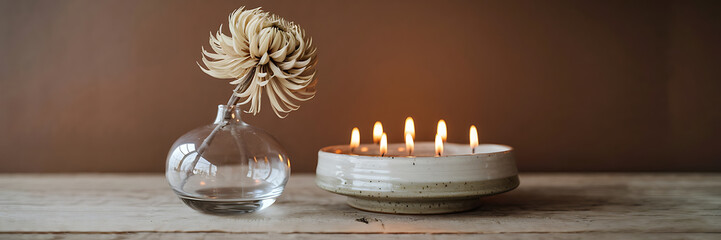 White flower in glass vase and burning candles in ceramic bowl on wooden table  rustic and cozy  warm and inviting  autumnal ambiance   