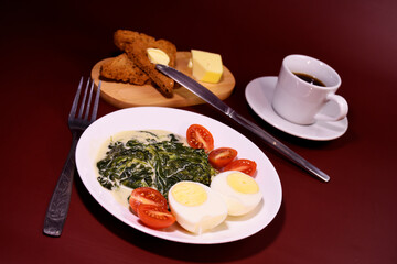 Healthy breakfast. Fresh boiled eggs with cherry tomatoes and spinach in cheese sauce. Coffee and buttered toast. Proper nutrition.
