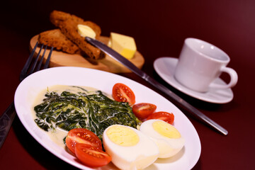 Healthy breakfast. Fresh boiled eggs with cherry tomatoes and spinach in cheese sauce. Coffee and buttered toast. Proper nutrition.