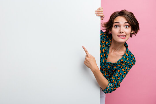Portrait of impressed woman wear print blouse indicating at promo on white wall empty space biting lips isolated on pink color background