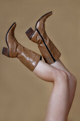 cowboy boots on bare female legs . pink background