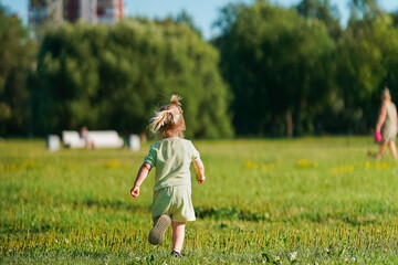 Fototapeta premium Caucasian joyful Little child girl runs on the green grass in the park in summer, the concept of a carefree childhood and freedom.