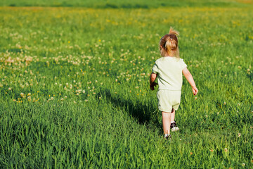 Caucasian joyful Little child girl runs on the green grass in the park in summer, the concept of a carefree childhood and freedom.