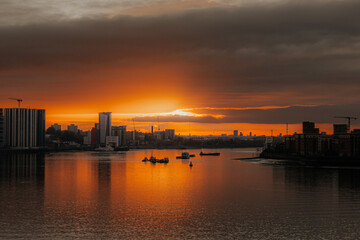 Fototapeta premium London skyline with a vibrant orange sunset reflecting off the River Thames, capturing the city’s evening ambiance.