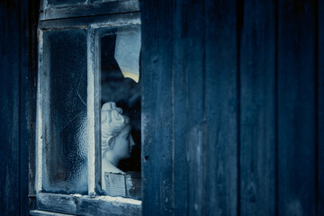 Mysterious window in abandoned building, illuminated with moody blue tones, evoking a haunting atmosphere