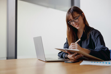 A dedicated professional woman is working diligently with her laptop and taking notes in a modern office environment