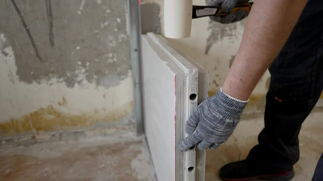 Construction worker installing plasterboard on metal profile using rubber mallet