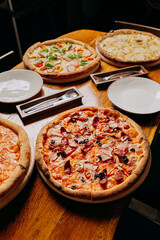 Assorted pizzas on a rustic wooden table, ready to serve with plates and cutlery