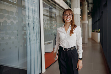 A smiling woman in stylish business attire confidently walks through a modern office filled with innovative design