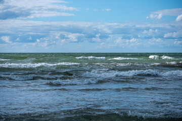 Waves gently rolling onto the shoreline under a cloudy sky at midday near a tranquil coastal area