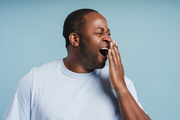 Sleepy bored African American guy yawning with eyes closed isolated on blue