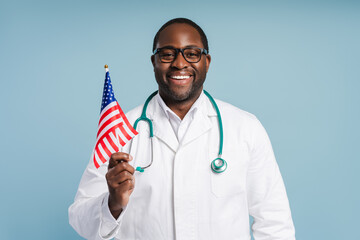 Happy African American doctor in white coat standing with USA flag in studio