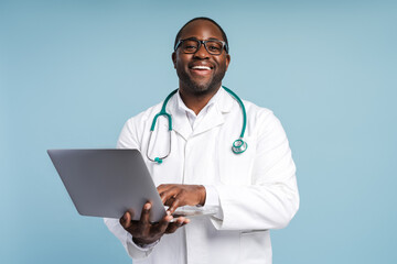 Happy African American doctor in eyeglasses holding laptop looking at camera in studio