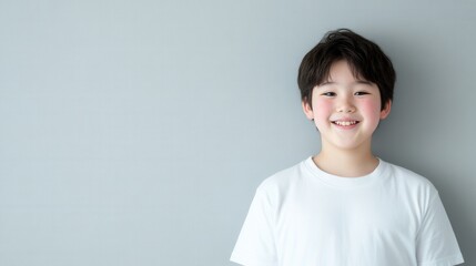 灰色の背景に、白いシャツを着て明るく笑っている、うれしそうなアジア人の子供