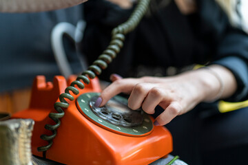 Close up of hand holding old orange rotary telephone with telephone on wooden retro table. Vintage rotary telephone concept.