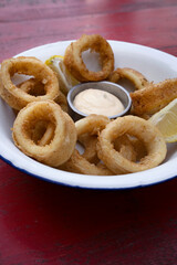 Deep fried seafood. Top view of delicious fried squid rings with lemon and a dipping sauce in a white bowl.