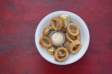 Deep fried seafood. Top view of delicious fried squid rings with lemon and a dipping sauce in a white bowl.