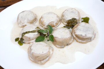 Italian food. Pasta. Closeup view of mozzarella cheese and ham sorrentinos with cream and pesto sauce, in a white dish.