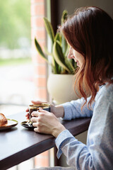 Attractive woman in blue dress sitting at table and enjoying cup of coffee in cafe