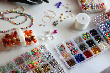 Hand figurine, colorful friendship bracelets, necklaces, various beads and DIY supplies on the table. Making jewelry at home. Selective focus.