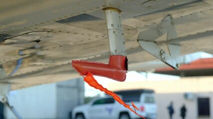 Remove before flight pitot tube cover under the wing of a parked airplane, protection for air speed measuring instrument, red warning flag on aircraft, closeup view