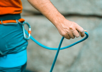 A young man belays for rock climbing in the mountains outdoors, an athlete controls on a rope during a workout, goes mountain climbing on a sunny day, close-up.