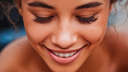 Obraz premium A close-up of a young woman with curly brown hair and long lashes, showcasing her joyful smile and glowing skin under soft natural light.