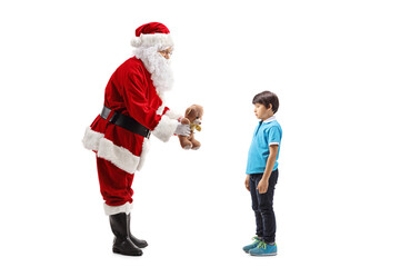Full length profile shot of Santa Claus giving a teddy bear to a boy