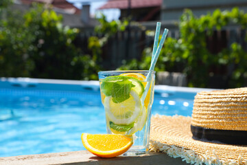 Tasty cocktail in glass and straw hat near swimming pool outdoors