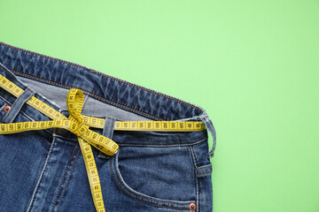 Jeans and measuring tape on light green background, top view. Space for text