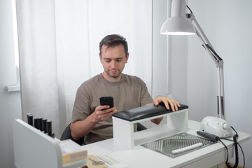 Manicure process for male nails in a beauty salon. Concept hand care and natural Manicure for man. Guy using a smartphone during procedure. 