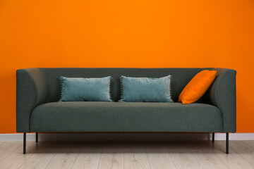 Stylish sofa with pillows near orange wall indoors